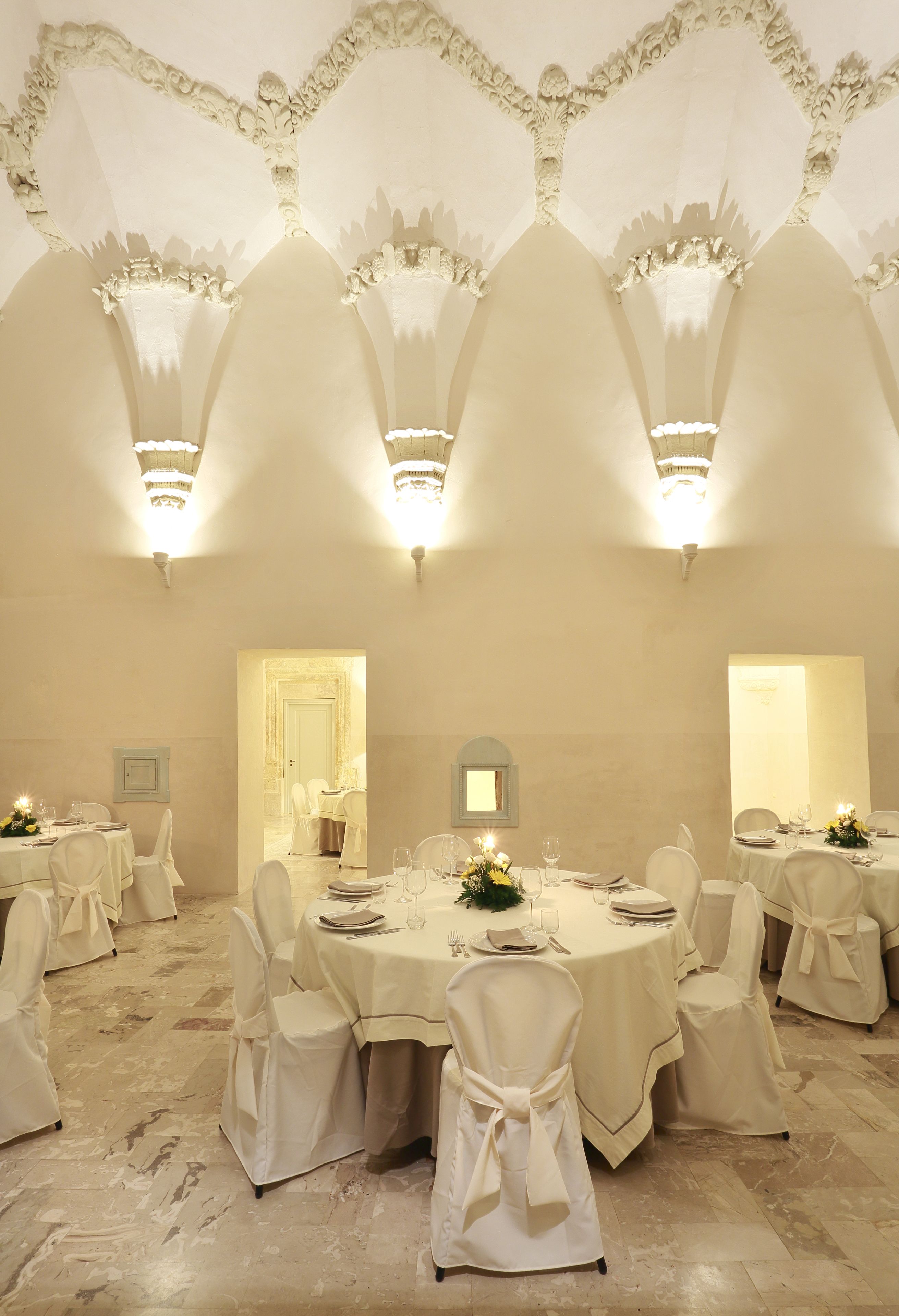 A banquet hall with round tables, white chairs, and chandeliers.