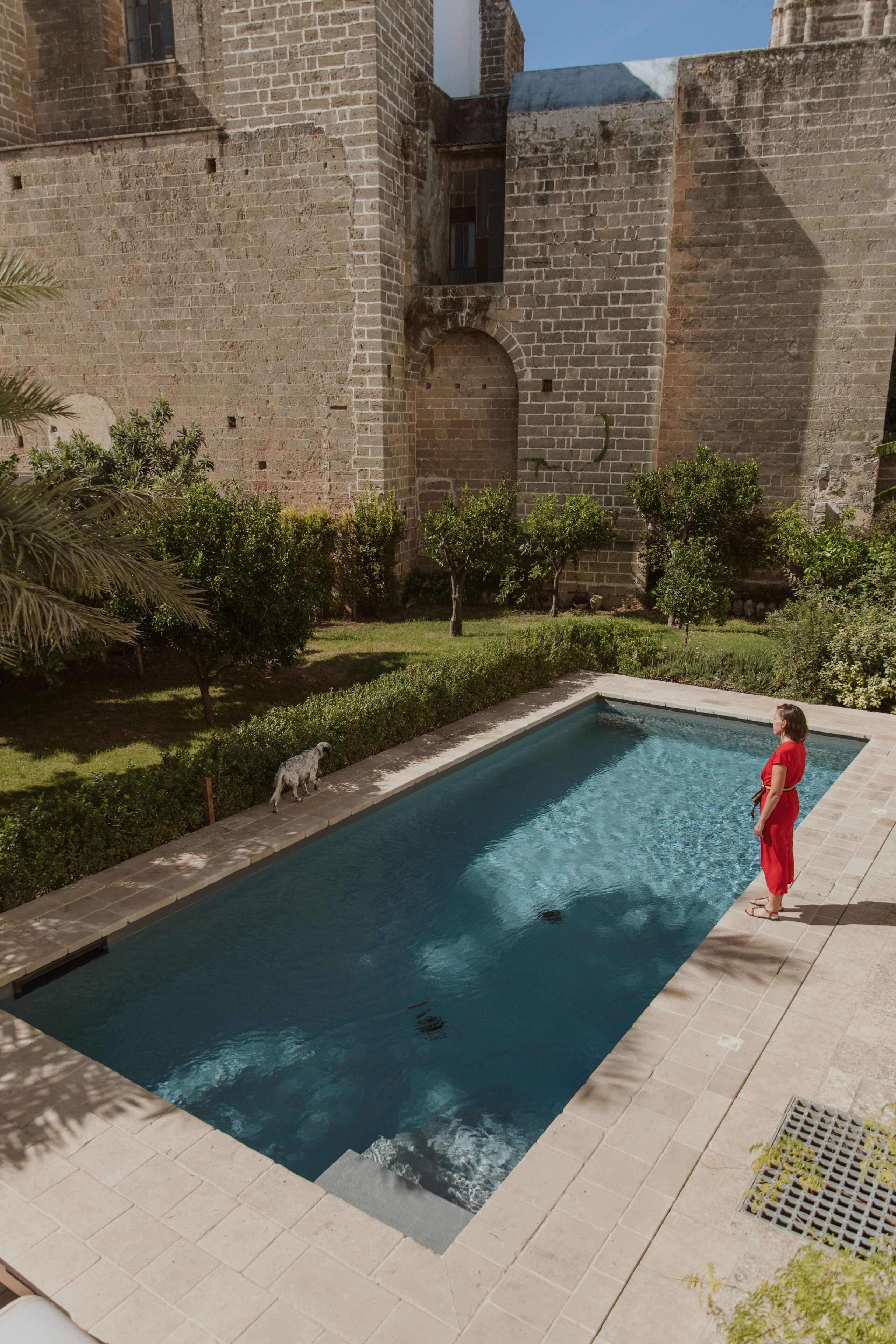 A swimming pool adjacent to a historic building with a brick facade and arched windows.
