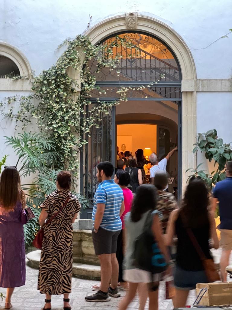 Un groupe de personnes se trouve devant un bâtiment dont l’entrée est richement décorée et qui est surmonté d’un escalier.