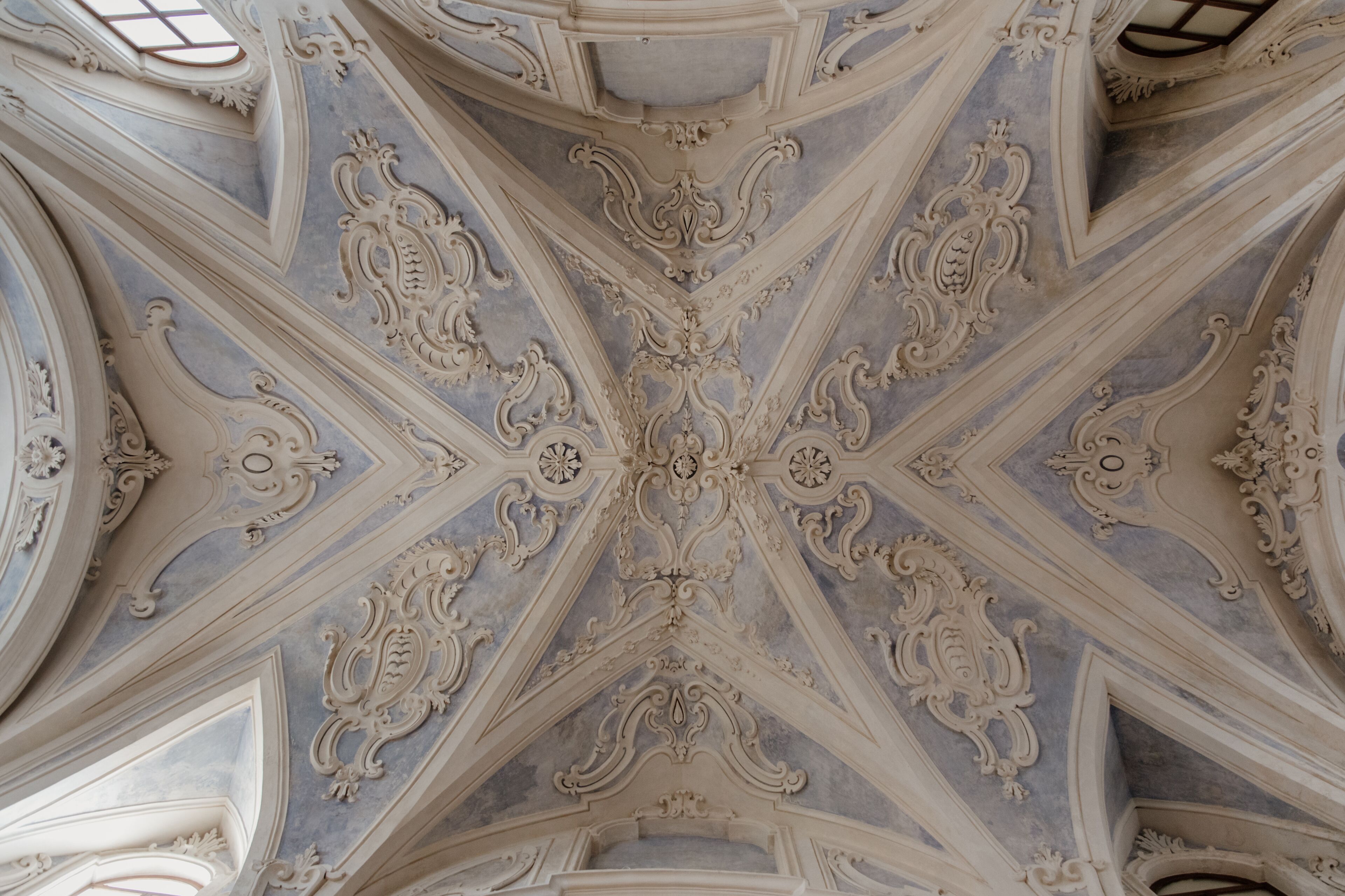 Een plafond met gedetailleerde, symmetrische en versierde architectuur.
