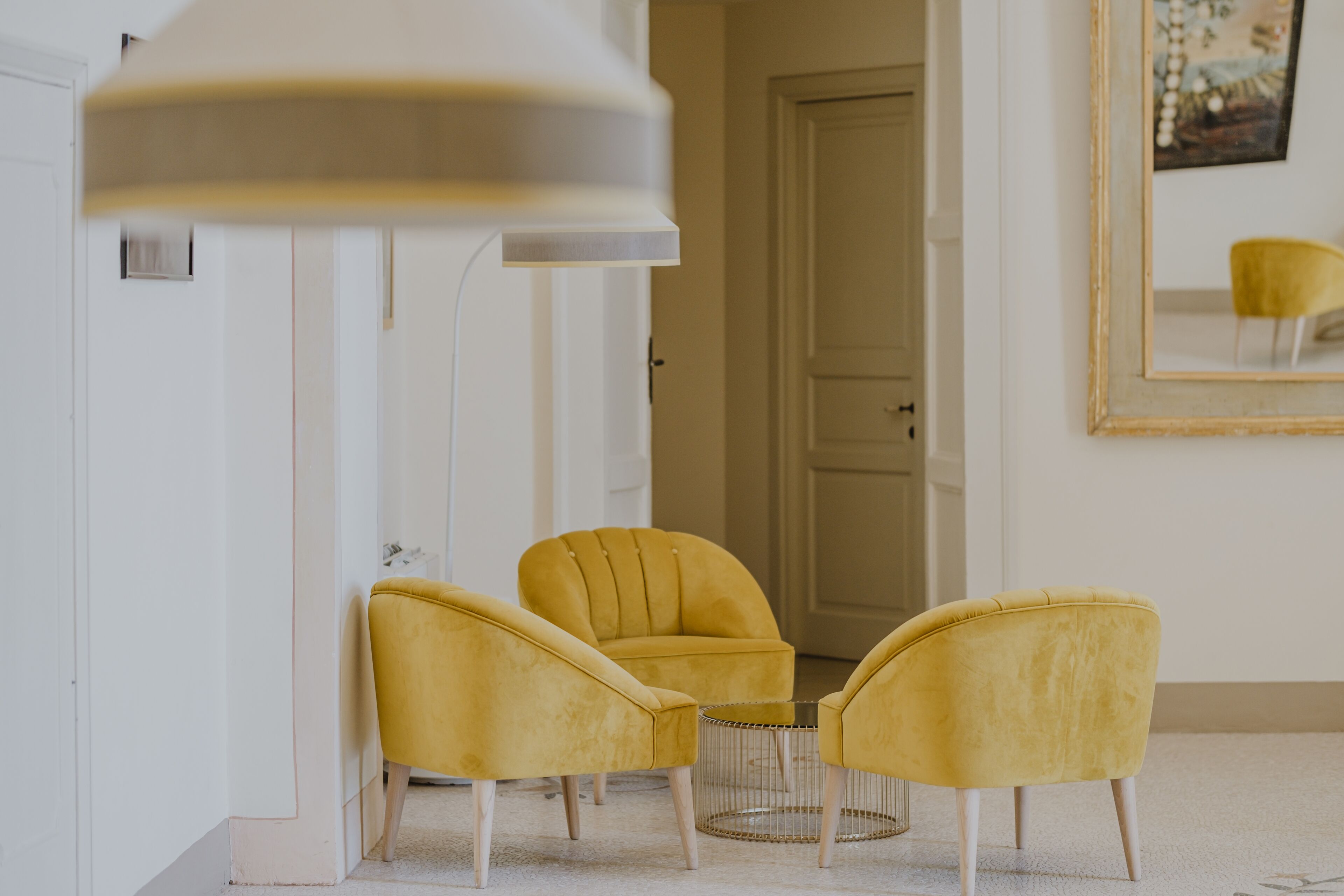 A room with three yellow chairs, a round table, and a large mirror on the wall.