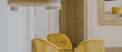 A room with three yellow chairs, a round table, and a large mirror on the wall.