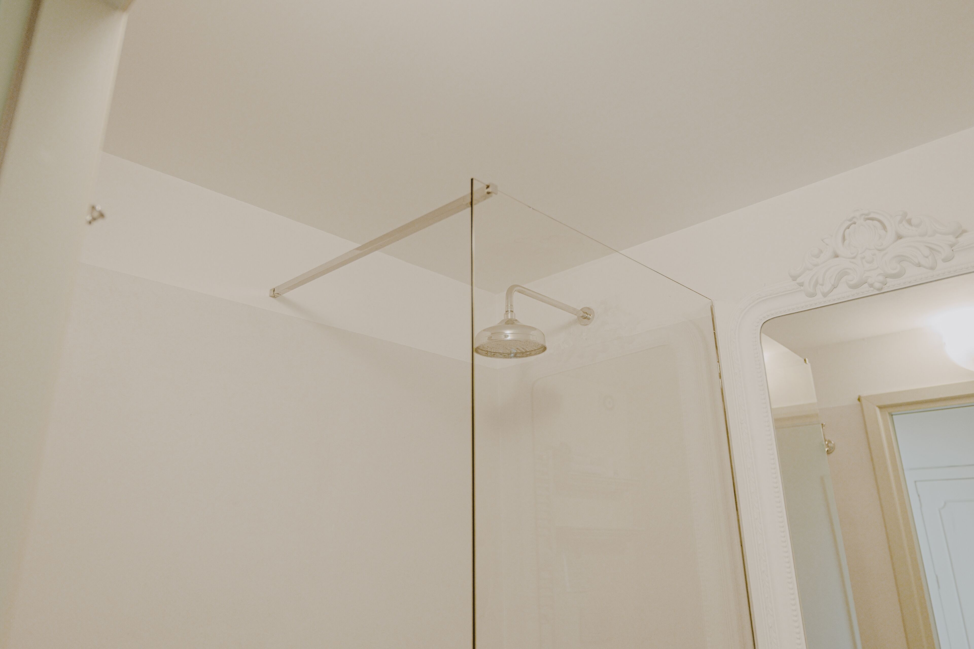Une salle de bain avec une douche à parois de verre, un plafond blanc et une porte visible au fond.