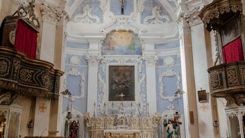 An ornate church interior with a red carpet leading to the altar, wooden pews, and elaborate ceiling decorations.