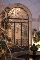 Una reja de hierro forjado con diseños intrincados, una fuente de piedra y un jardín bien cuidado con diversas plantas.
