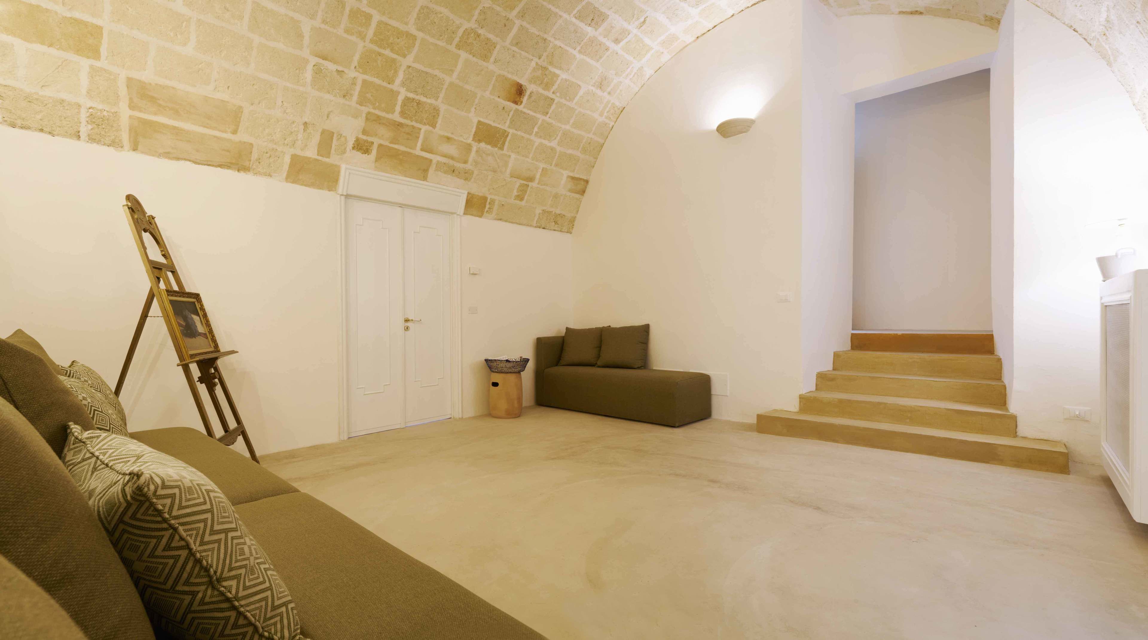 Ein geräumiger Raum mit hoher, gewölbter Decke, einer Treppe, einem Sofa und einer an der Wand lehnten Leiter.