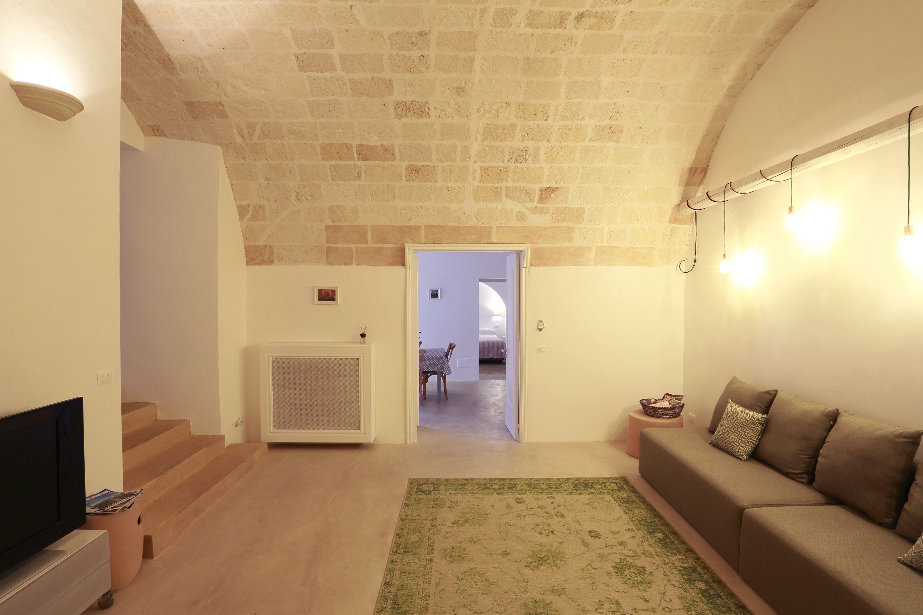 A living room with a TV, sofa, and a staircase leading to another room.