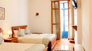 Habitación de hotel con dos camas, piso de madera, televisor montado en la pared y una puerta que da al exterior.
