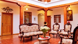 Un vestíbulo amplio con muebles ornamentados, una mesa redonda central con un jarrón de flores y un balcón con barandillas de madera.