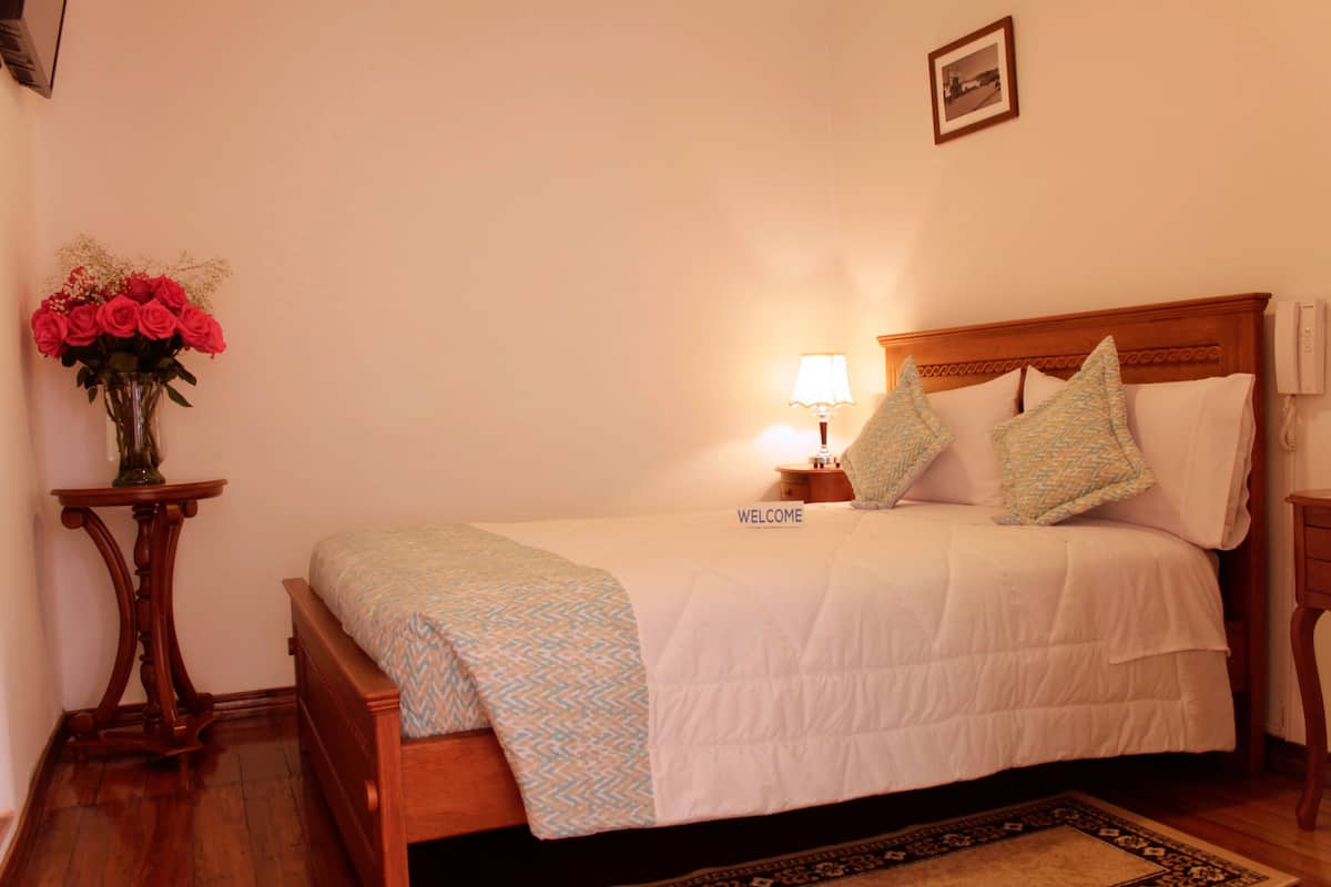 A neatly made bed with a 'WELCOME' sign, a bedside lamp, and a vase of red roses on a wooden nightstand.