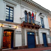En hotelfasadé med et skilt, der siger "Casa Hotel Las Plazas", altaner med flag og lukkede skodder.