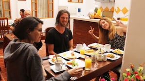 Un comedor con mesas y sillas de madera, y una variedad de alimentos para el desayuno, incluyendo platos, vasos y zumo de naranja.