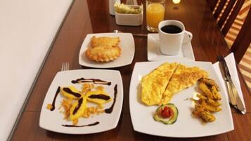 Une table dressée pour le petit-déjeuner avec une assiette de crêpes, une assiette de viennoiseries et une assiette contenant une omelette, des légumes et une tranche de tomate.