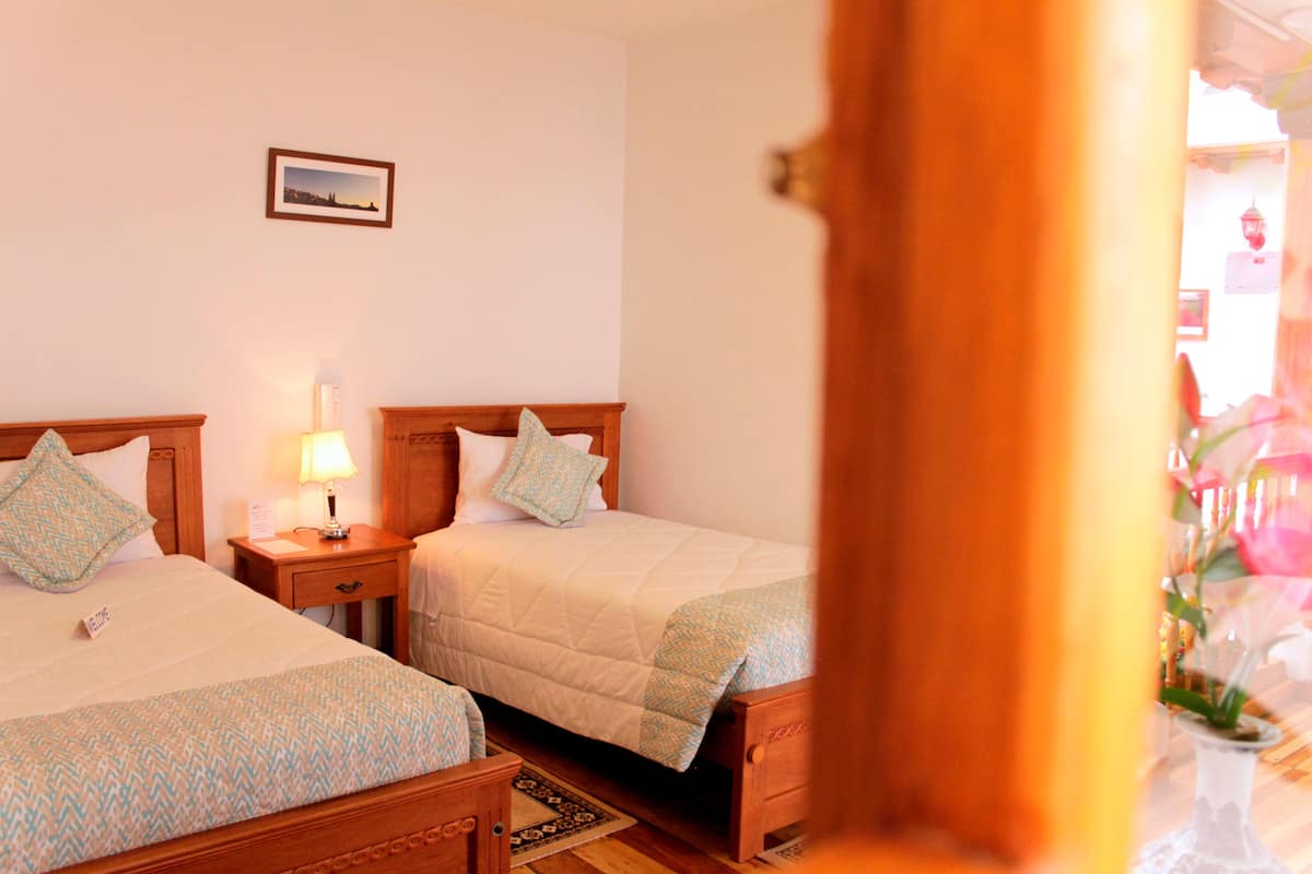 A hotel room with two wooden beds, each with a pillow and a bedside table with a lamp.