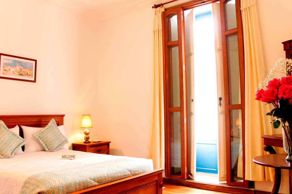 A hotel room with a bed, a nightstand, a lamp, a vase with flowers, and a painting on the wall.