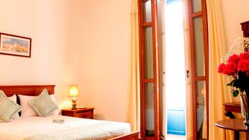A hotel room with a bed, a nightstand, a lamp, a vase with flowers, and a painting on the wall.