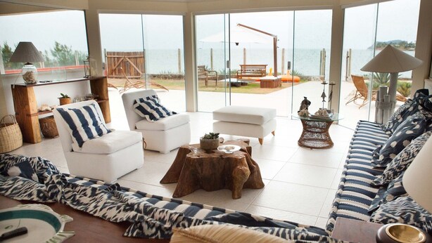 A spacious living area with a large glass door leading to an outdoor patio. There are two white sofas, a wooden coffee table, and a wicker side table. - Casa do Mar Buzios (Búzios)