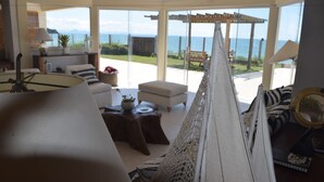 A spacious living area with a large window overlooking the sea, a cozy seating arrangement, and a decorative hanging piece. - Casa do Mar Buzios (Búzios)