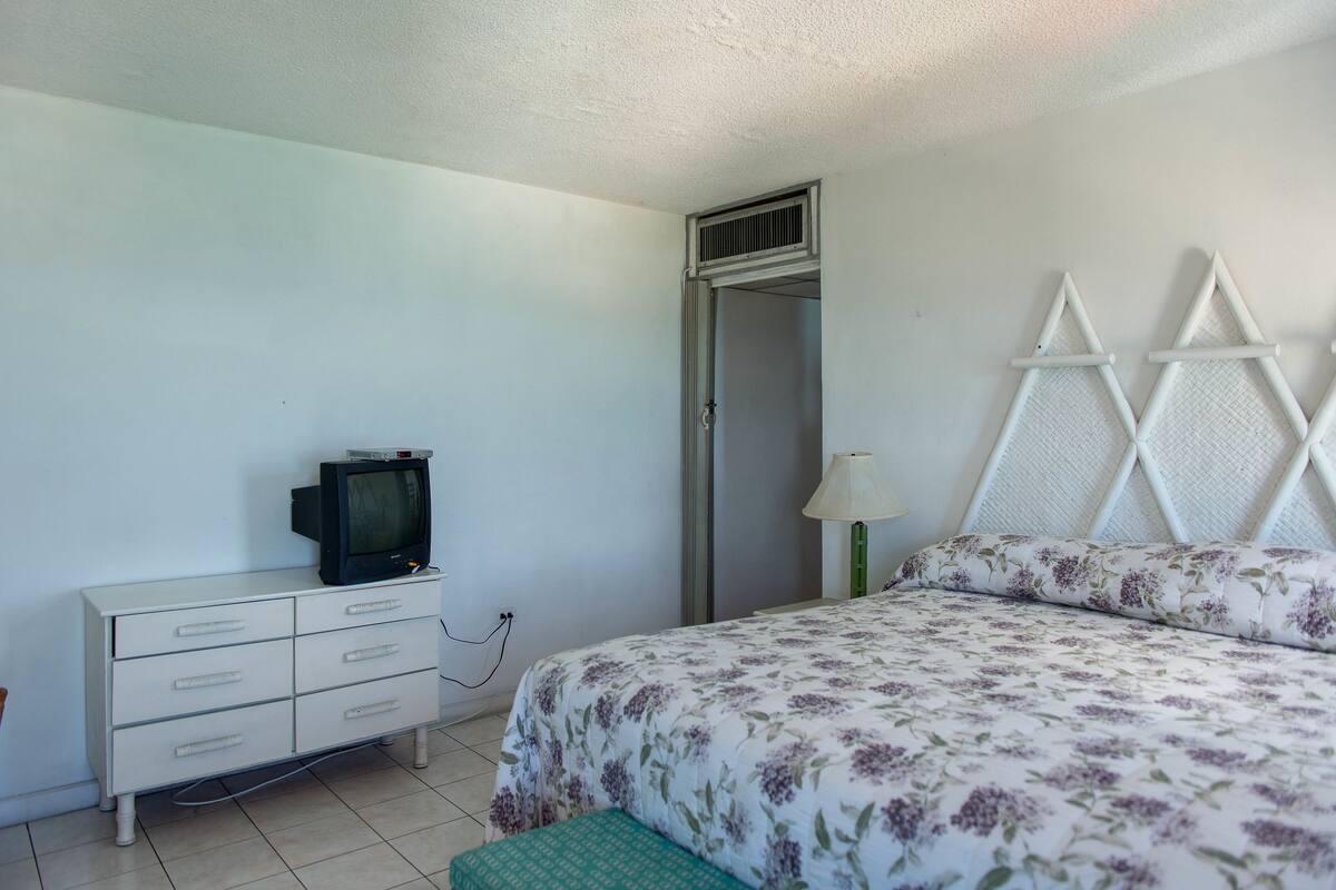 A bedroom with a bed, a dresser, a television, and a window.