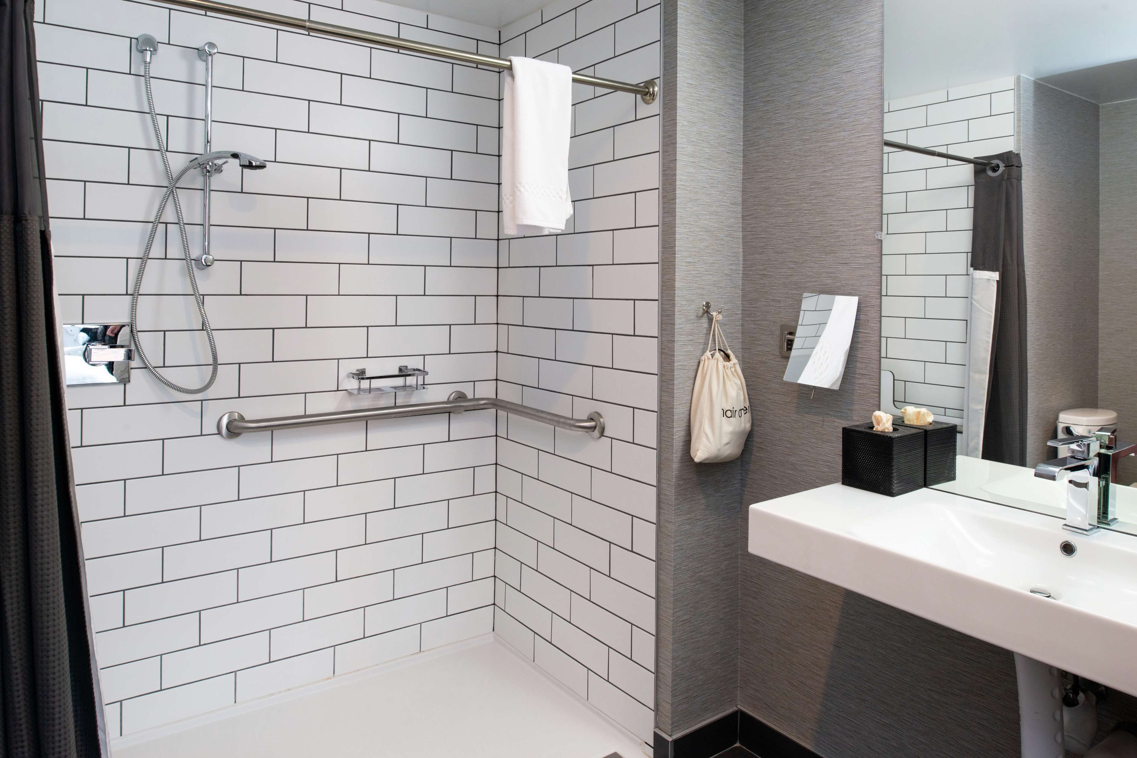 A modern bathroom with white subway tiles, a glass shower enclosure, a white sink, and a mirror.