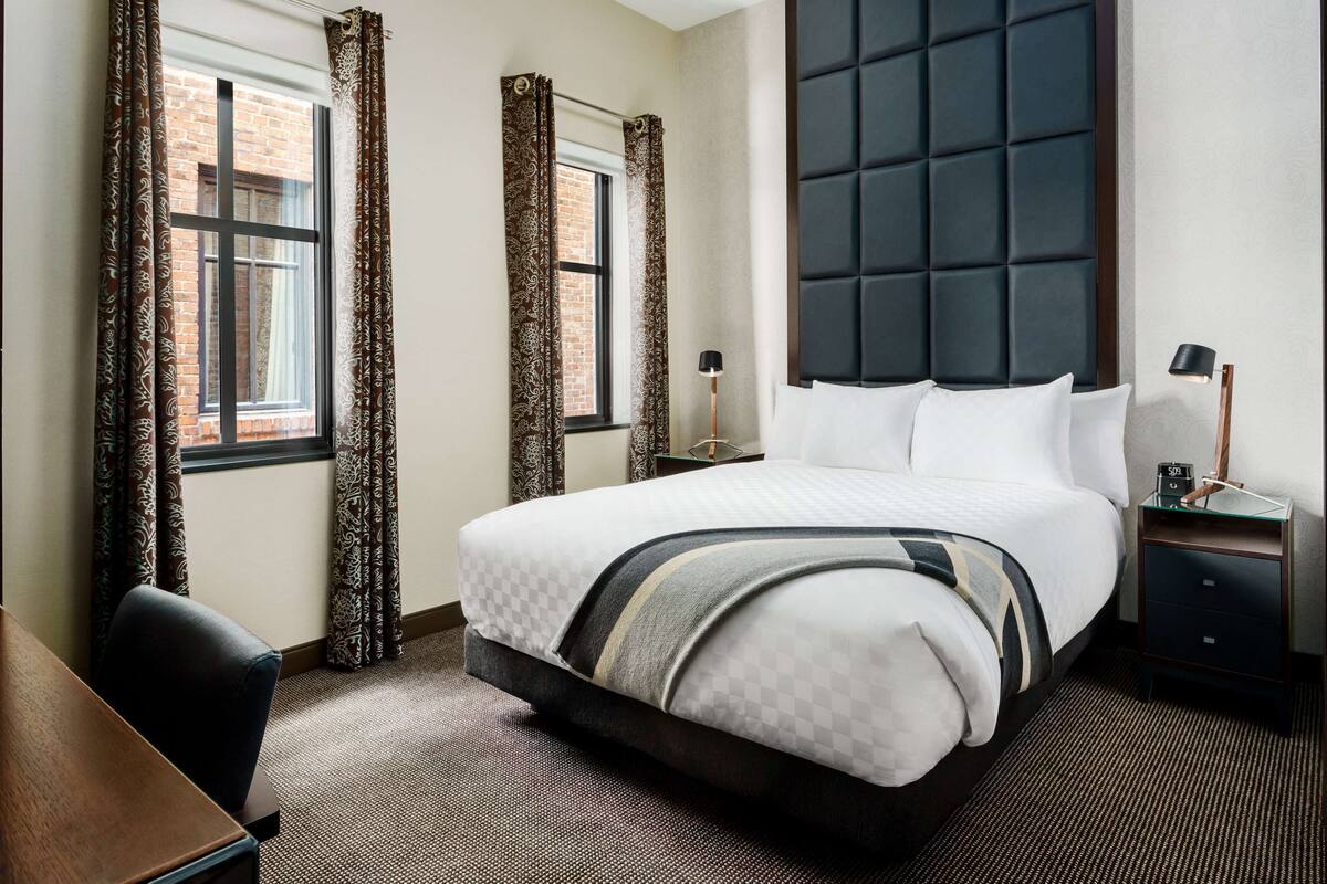 Ein Hotelzimmer mit einem großen Bett, einem Schreibtisch und einem Nachttisch mit Lampe.