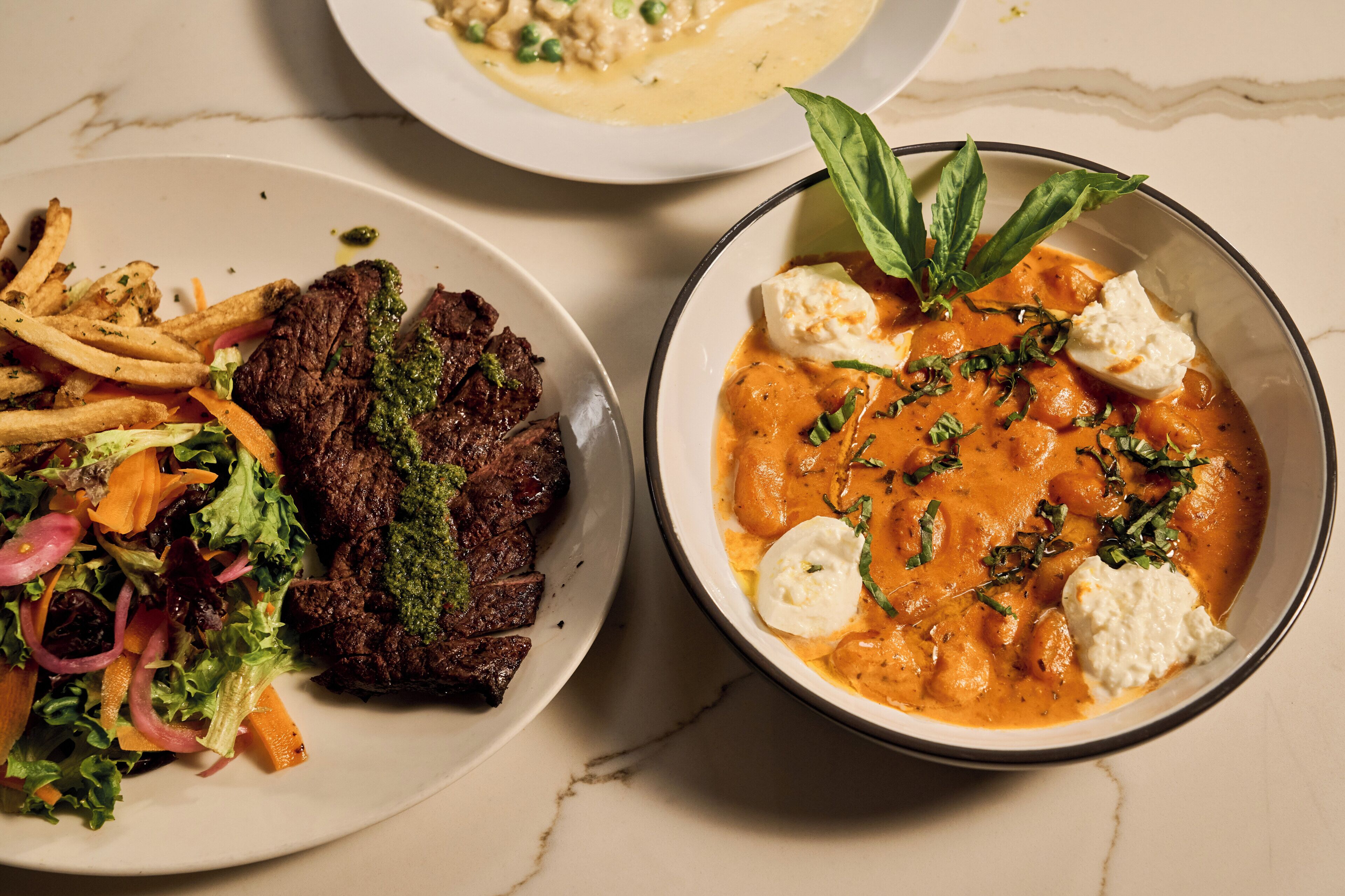 A plate of steak with fries and a salad, and a bowl of soup with a garnish.