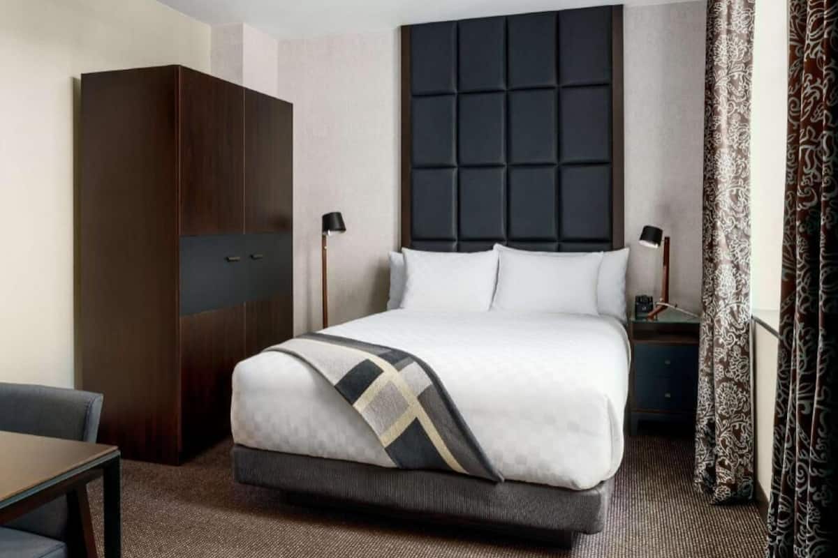Ein Hotelzimmer mit Bett, Kleiderschrank, Schreibtisch und Nachttisch.