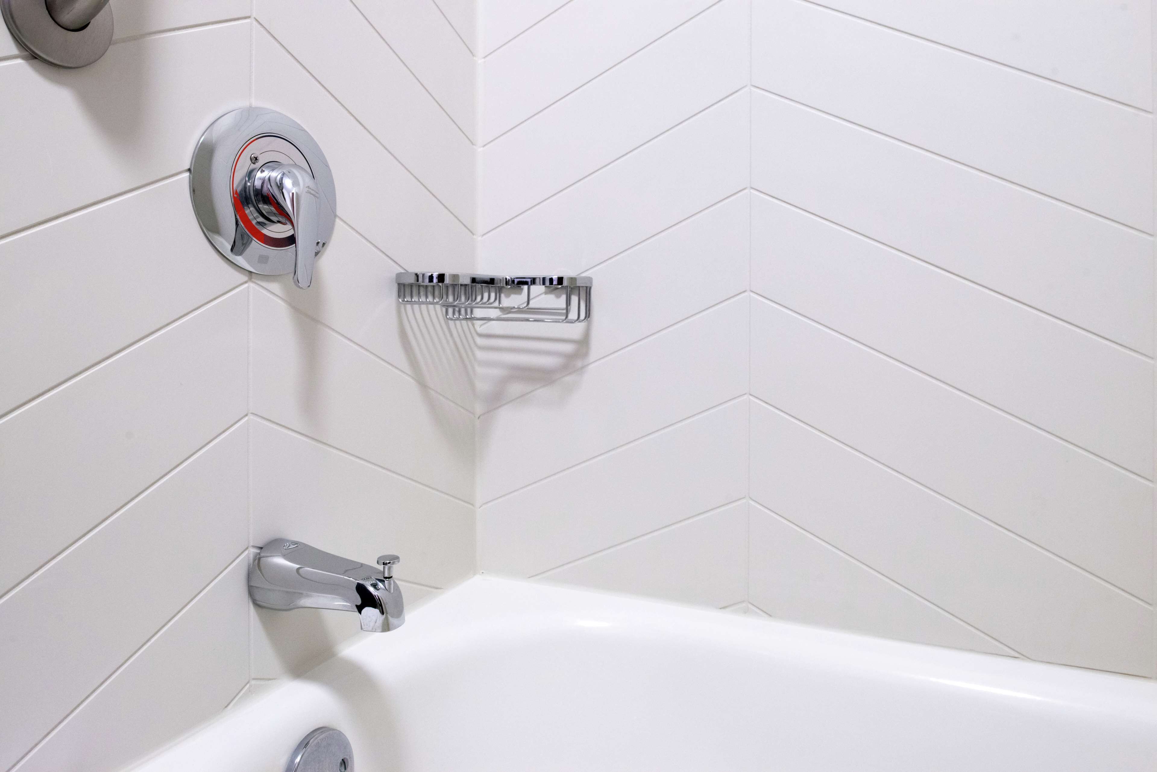 Ein modernes Badezimmer mit einer weißen Badewanne, Chromarmaturen und einer Wand mit Zickzackmuster-Fliesen.