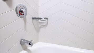 A modern bathroom with a white bathtub, chrome fixtures, and a chevron-patterned tile wall.
