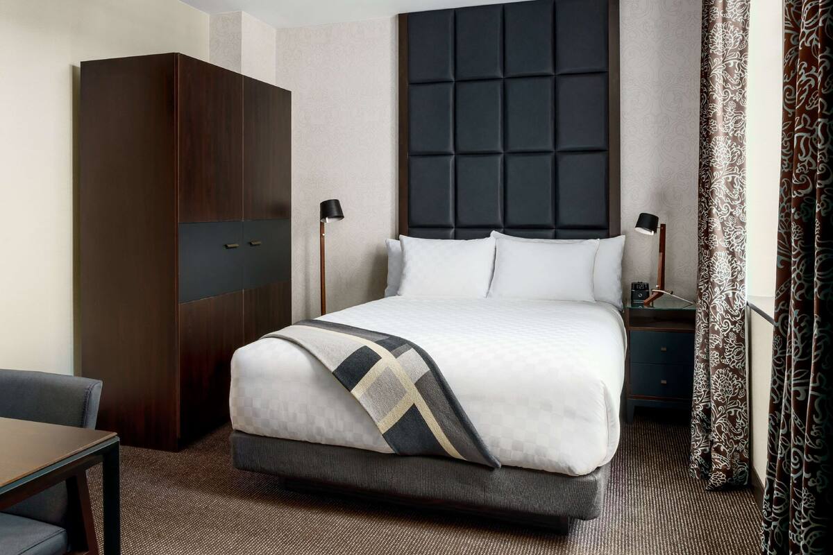 Ein Hotelzimmer mit einem großen Bett, einem Kleiderschrank, einem Nachttisch und einer Lampe.