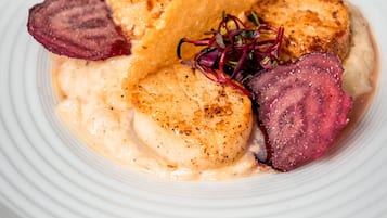 A white plate with a seafood dish, including scallops and a slice of meat, garnished with a beet slice and microgreens.
