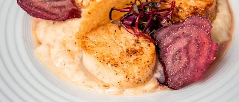 A white plate with a seafood dish, including scallops and a slice of meat, garnished with a beet slice and microgreens.