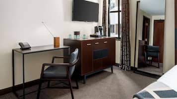 A hotel room with a desk, chair, TV, wardrobe, and a bed.