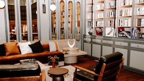 Una sala de estar acogedora con un sofá de cuero marrón, una silla de madera y una mesa de centro. Se observa una estantería llena de libros y objetos decorativos.