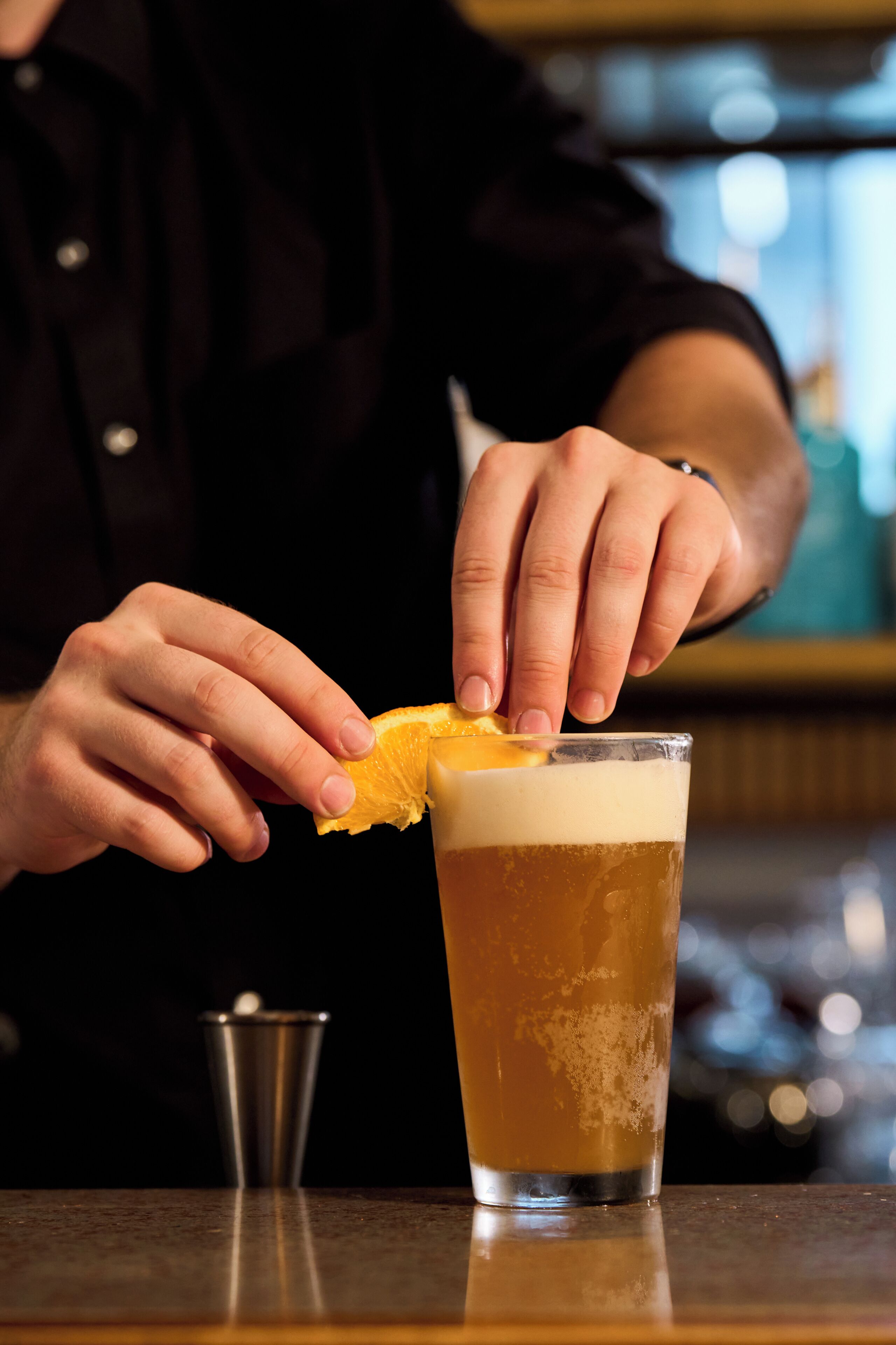 A person holding an orange slice over a glass of beer.