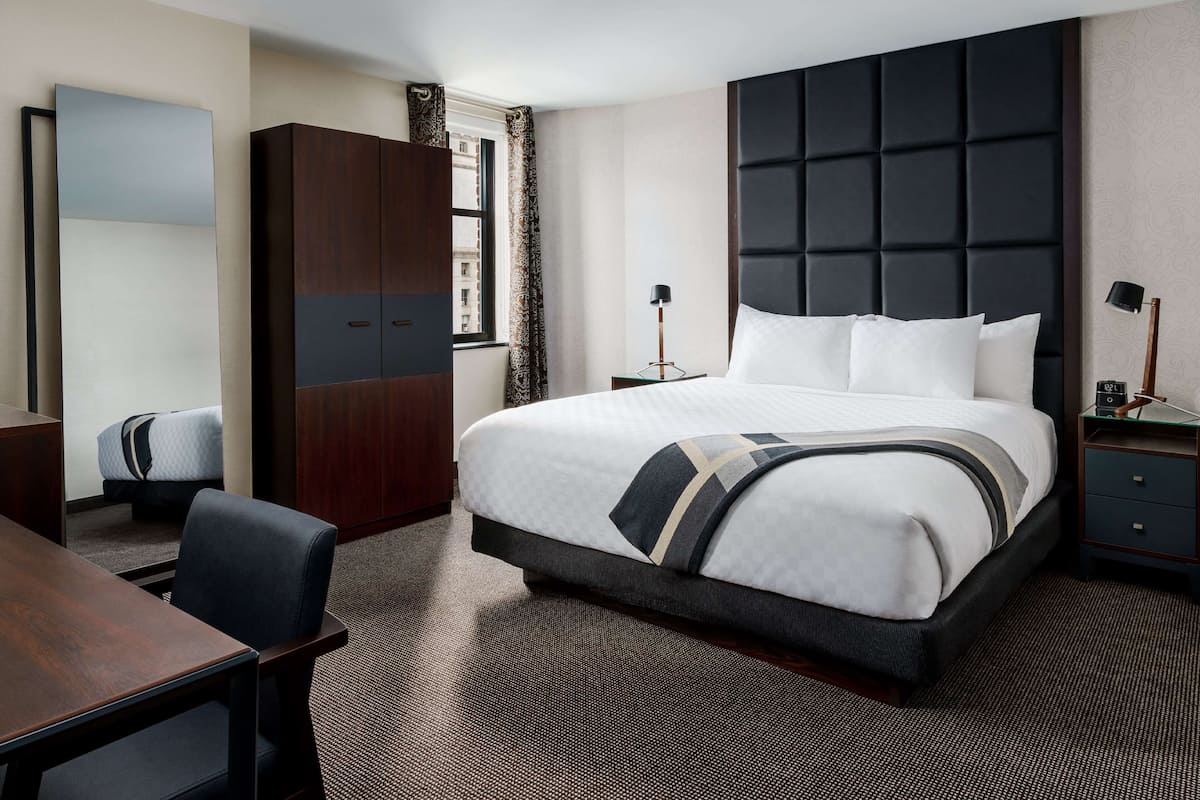 Ein Hotelzimmer mit einem großen Bett, einem Schreibtisch, einem Kleiderschrank und einem Nachttisch mit einer Lampe.