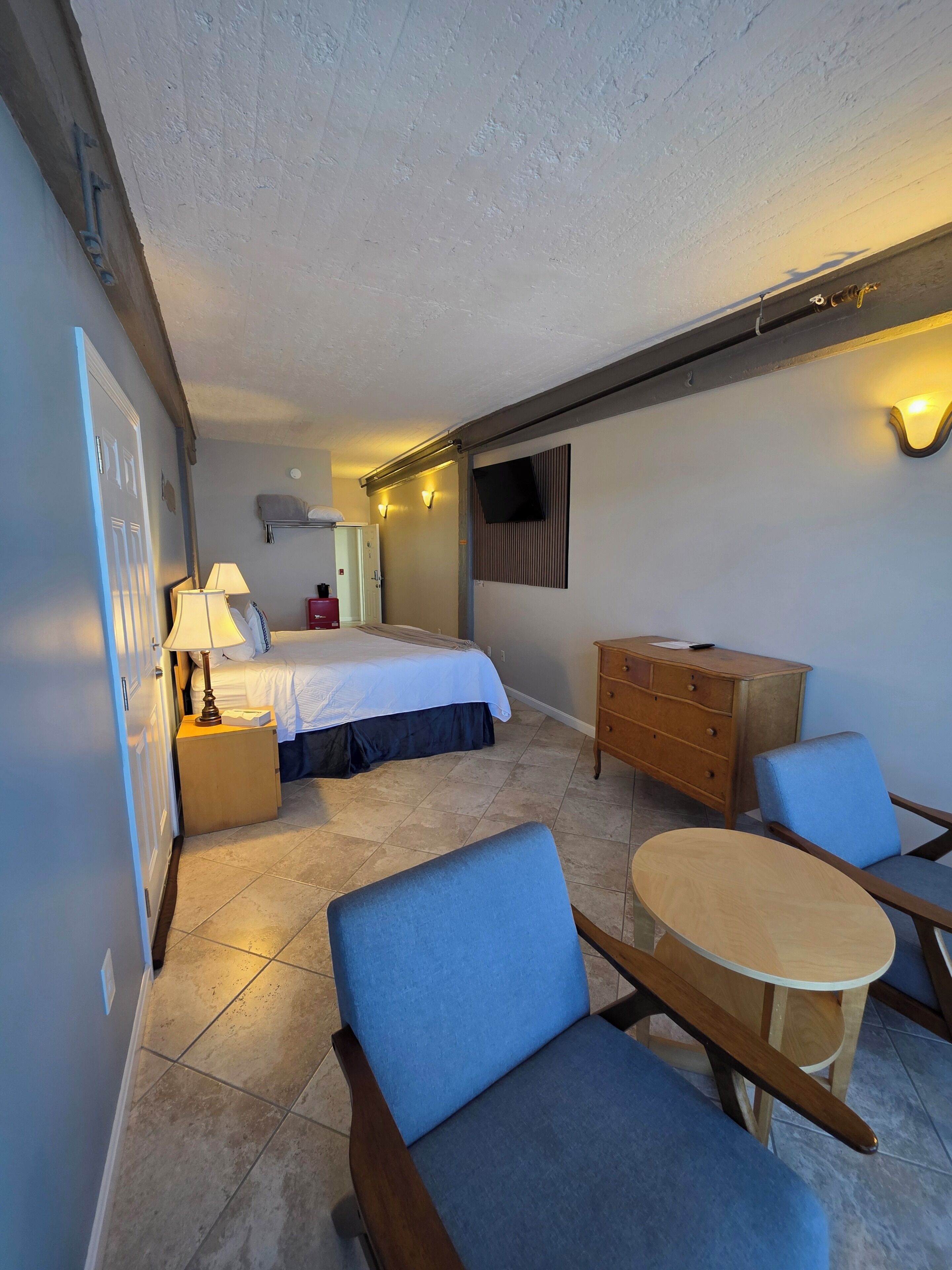 A hotel room with a bed, bedside table, lamp, dresser, and a small round table with chairs.
