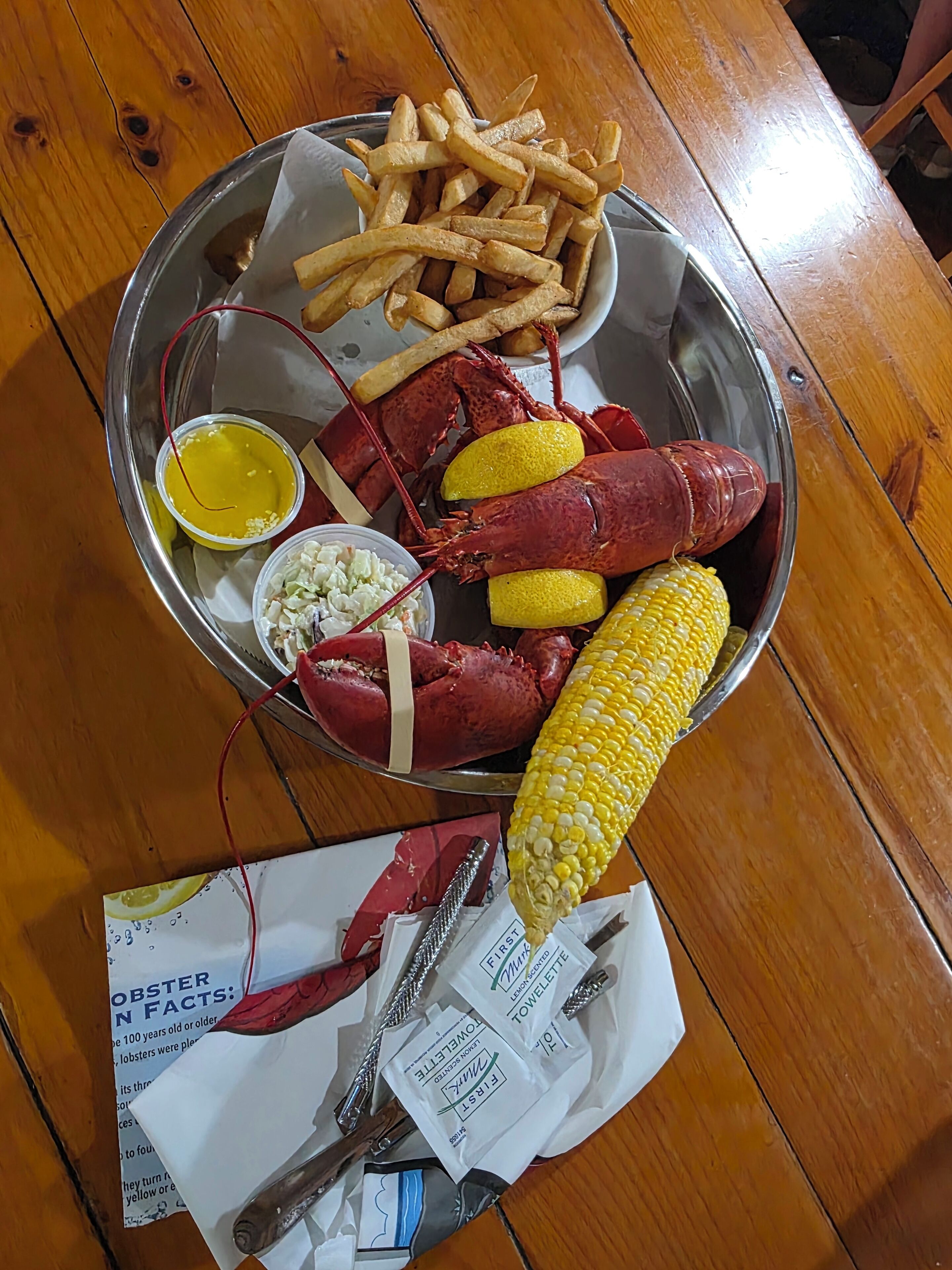 A meal consisting of lobster, corn on the cob, French fries, and coleslaw on a metal tray.