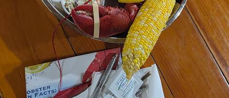 A meal consisting of lobster, corn on the cob, French fries, and coleslaw on a metal tray.