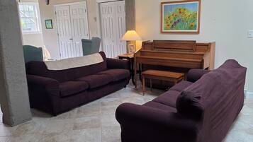 Un salon spacieux comprenant un grand canapé, un canapé plus petit, un piano en bois et une lampe.