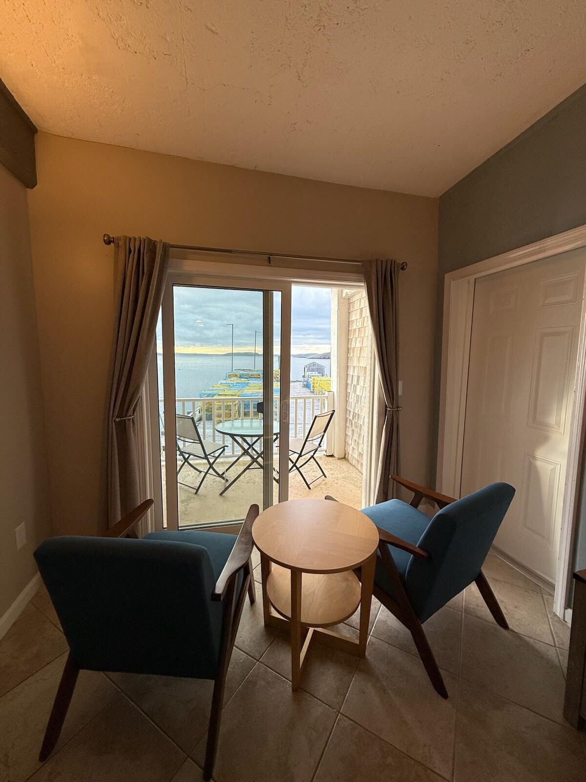 Une pièce dotée d’une porte-fenêtre coulissante donnant sur un balcon, de deux chaises bleues, d’une petite table ronde et d’une porte blanche.