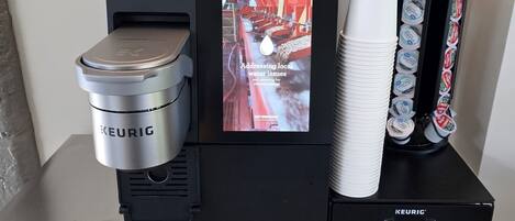 Une machine à café Keurig dotée d’un écran numérique, d’un moulin à café et d’une pile de gobelets jetables.