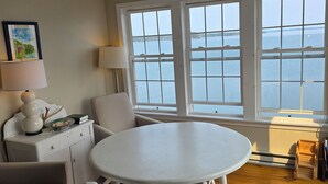 A room with a white table and chairs, a sofa, a lamp, and a view of the sea through large windows. - The Inn on the Wharf (Lubec)