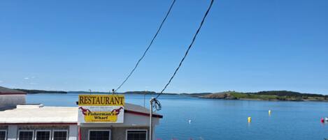A waterfront restaurant with a dock extending into a calm lake, surrounded by hills.