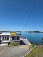 Un restaurante frente al agua con un muelle que se adentra en un lago tranquilo, rodeado de colinas.
