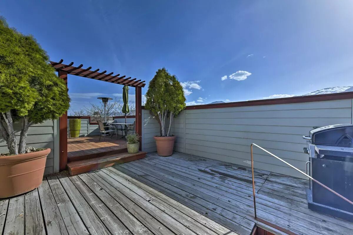 A wooden deck with a pergola, potted plants, and a barbecue grill.