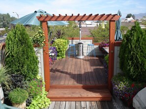 Una terraza de madera con una pérgola, sillas azules y una mesa.