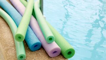 Un espace aménagé au bord de la piscine, avec plusieurs bouées en mousse de couleurs vives disposées sur une surface texturée.