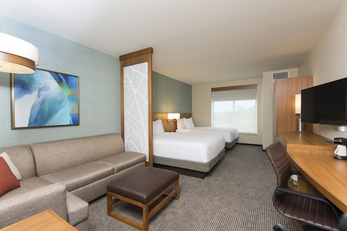 Une chambre d’hôtel avec un canapé, deux lits, un bureau et une télévision.