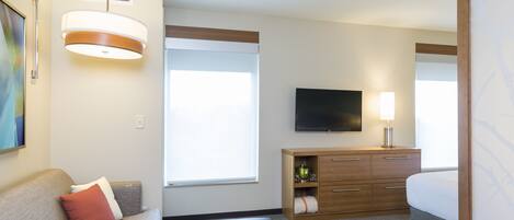 A hotel room with a sofa, a wooden cabinet, a flat-screen TV, and a window.